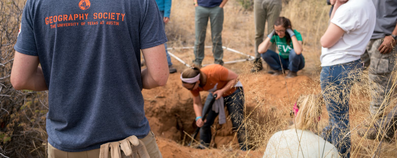 students and professors watching a student digging for fossils